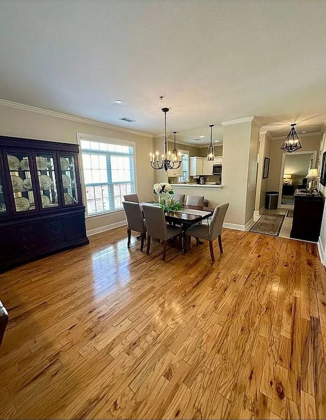 dining space featuring a chandelier, ornamental molding, and light hardwood / wood-style flooring