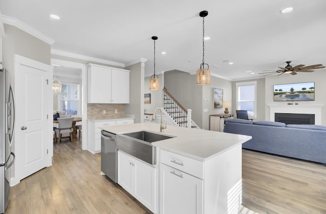 kitchen with light wood finished floors, a sink, appliances with stainless steel finishes, crown molding, and tasteful backsplash