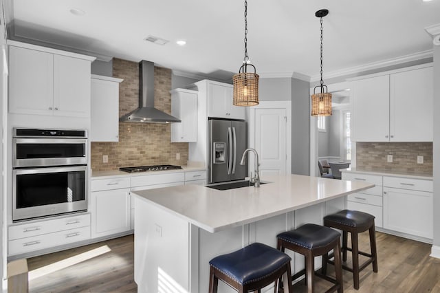 kitchen with crown molding, wall chimney range hood, wood finished floors, stainless steel appliances, and a sink