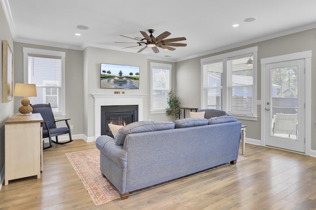 living area with a glass covered fireplace, a ceiling fan, light wood finished floors, and ornamental molding