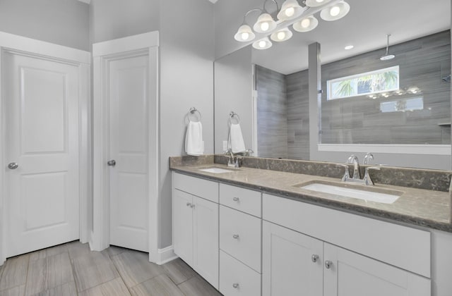 full bathroom featuring a sink, tiled shower, and double vanity