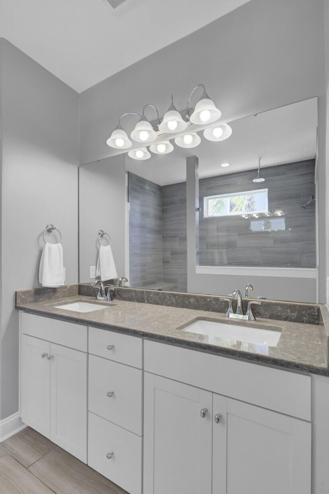 full bathroom featuring double vanity, tiled shower, baseboards, and a sink