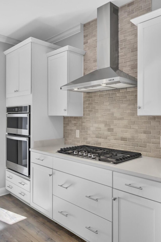 kitchen featuring white cabinetry, wall chimney exhaust hood, tasteful backsplash, and stainless steel appliances