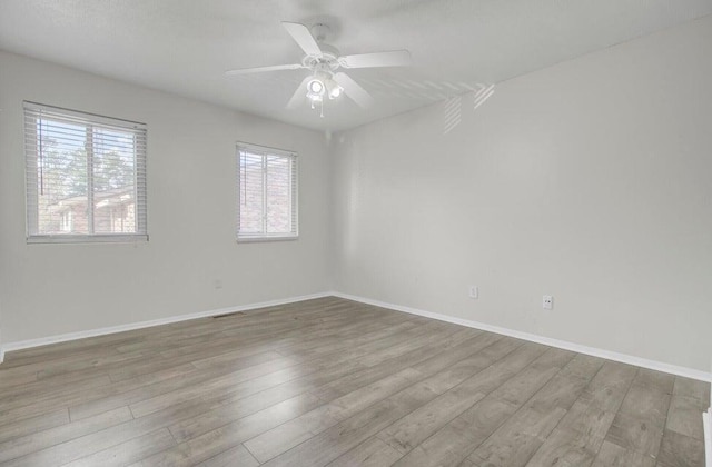 empty room with visible vents, ceiling fan, baseboards, and wood finished floors