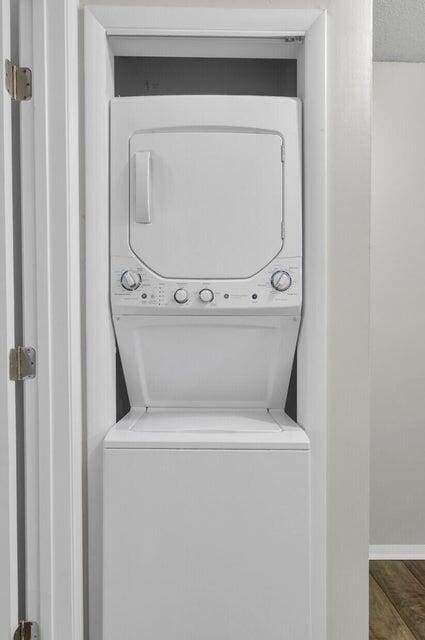 laundry area featuring stacked washer / drying machine, laundry area, baseboards, and wood finished floors