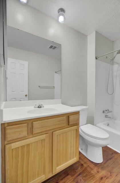 full bathroom with toilet, wood finished floors, vanity, visible vents, and washtub / shower combination