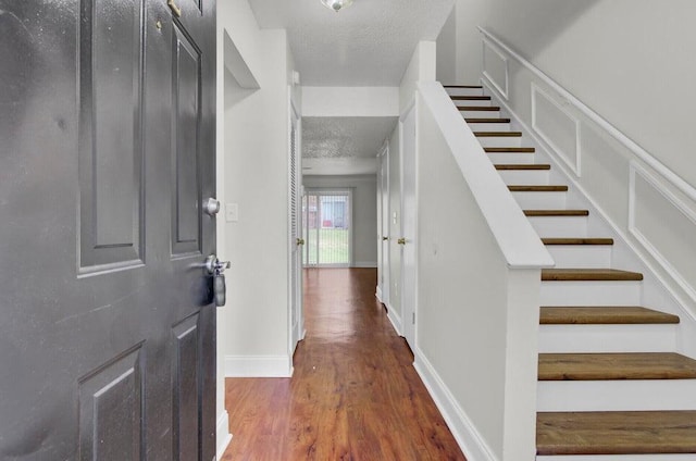 entrance foyer featuring a decorative wall, a textured ceiling, wood finished floors, baseboards, and stairs