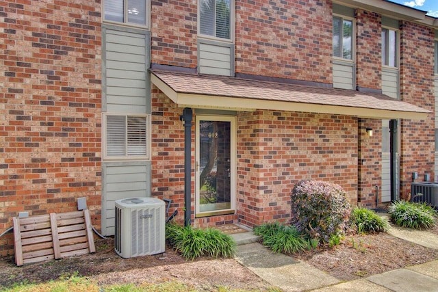 rear view of house featuring central air condition unit, roof with shingles, and brick siding