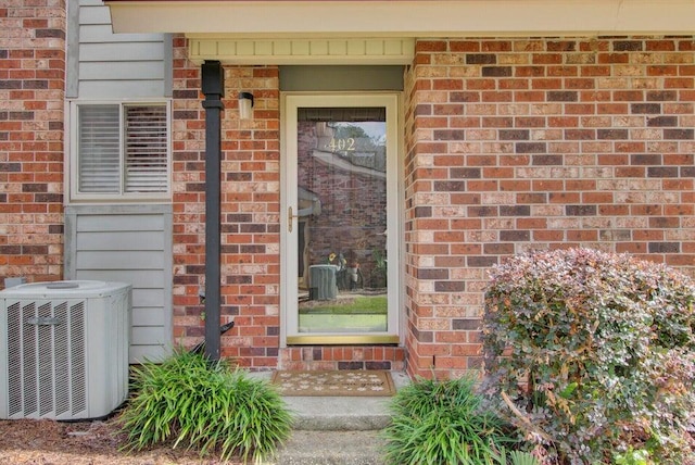 view of exterior entry with central AC and brick siding