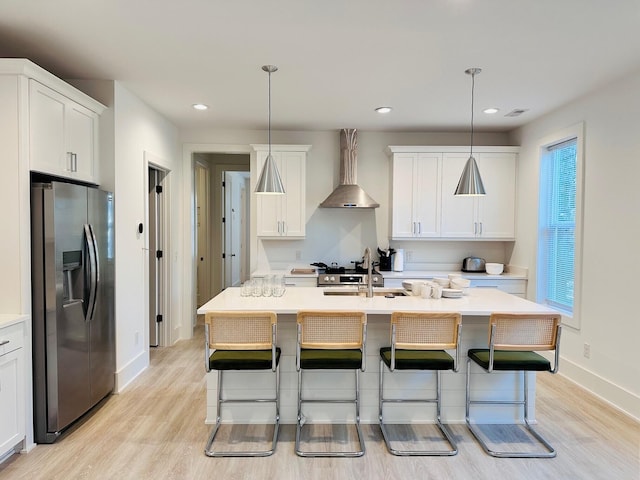 kitchen featuring wall chimney exhaust hood, stainless steel appliances, a kitchen island with sink, and pendant lighting