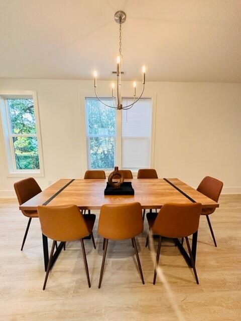 dining room with vaulted ceiling, plenty of natural light, a notable chandelier, and light hardwood / wood-style flooring