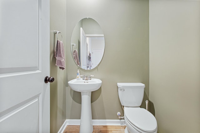 half bath with wood finished floors, toilet, and baseboards