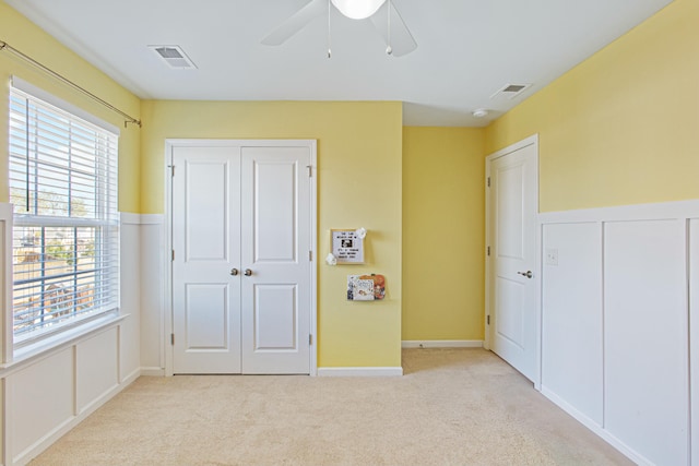 unfurnished bedroom featuring a decorative wall, wainscoting, visible vents, and light colored carpet