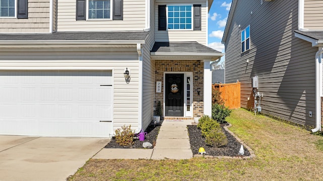 entrance to property with brick siding, a shingled roof, concrete driveway, an attached garage, and fence