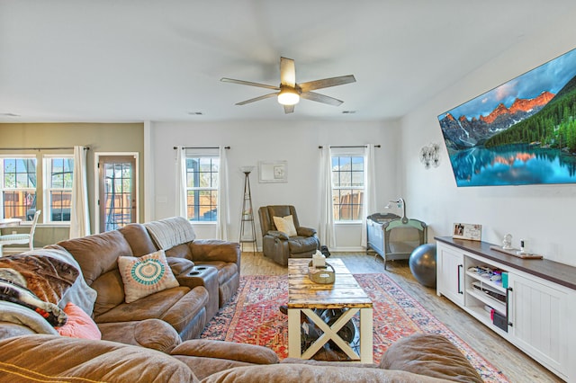 living area featuring light wood-style floors, plenty of natural light, visible vents, and a ceiling fan