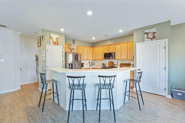 kitchen featuring stainless steel appliances, light countertops, light brown cabinetry, light wood finished floors, and tasteful backsplash