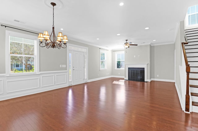 unfurnished living room with ceiling fan with notable chandelier, dark hardwood / wood-style floors, plenty of natural light, and ornamental molding