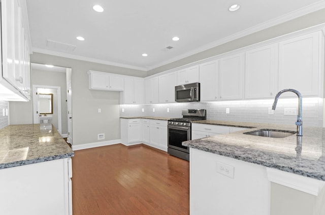 kitchen with dark wood-type flooring, dark stone countertops, ornamental molding, appliances with stainless steel finishes, and white cabinetry