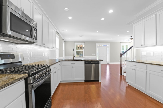 kitchen with kitchen peninsula, stainless steel appliances, dark wood-type flooring, sink, and white cabinets