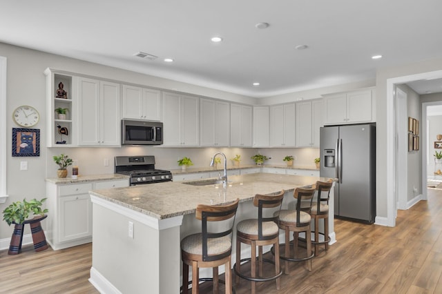 kitchen with sink, appliances with stainless steel finishes, a kitchen island with sink, light stone counters, and a kitchen bar