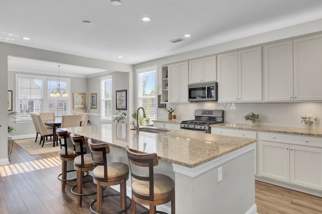 kitchen with an island with sink, stainless steel appliances, sink, and hanging light fixtures