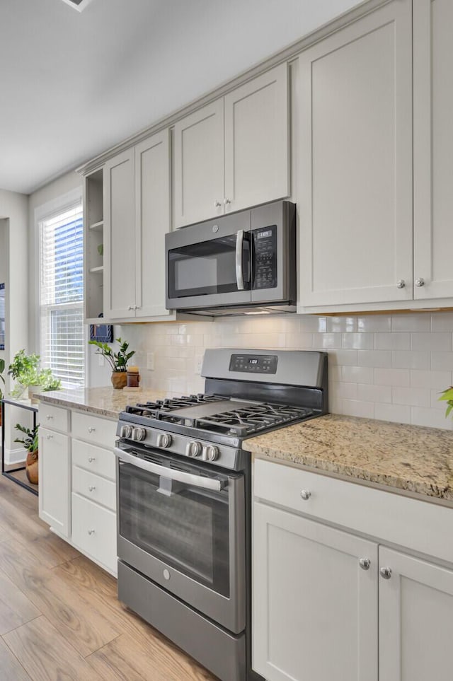 kitchen with stainless steel appliances, tasteful backsplash, light stone countertops, and light hardwood / wood-style floors