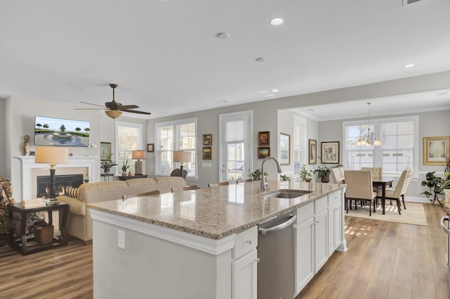 kitchen with white cabinetry, dishwasher, sink, an island with sink, and light stone countertops