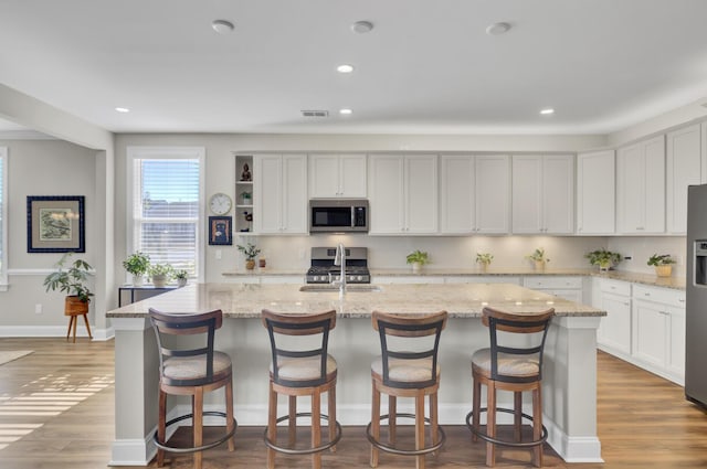 kitchen featuring a kitchen island with sink, light stone counters, a breakfast bar, and appliances with stainless steel finishes