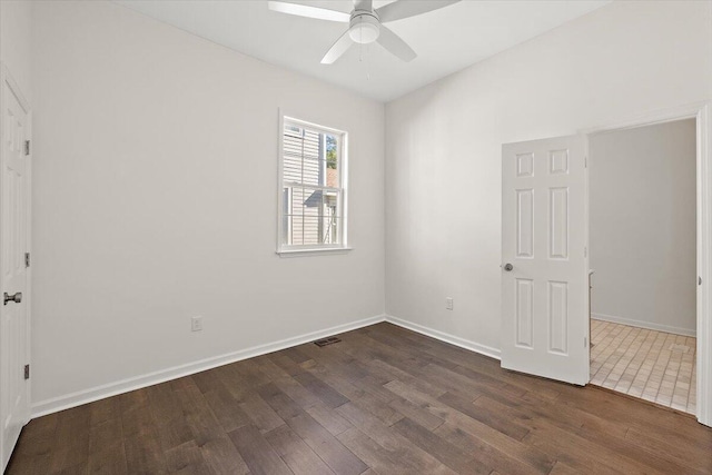 spare room with dark wood-style flooring, a ceiling fan, visible vents, and baseboards