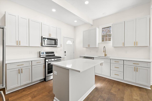 kitchen with a kitchen island, dark wood-type flooring, light countertops, a sink, and appliances with stainless steel finishes