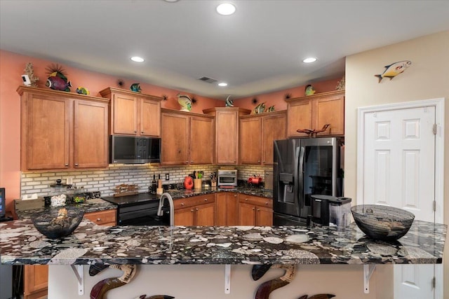 kitchen featuring stainless steel fridge with ice dispenser, backsplash, a kitchen bar, dark stone counters, and black range with electric cooktop