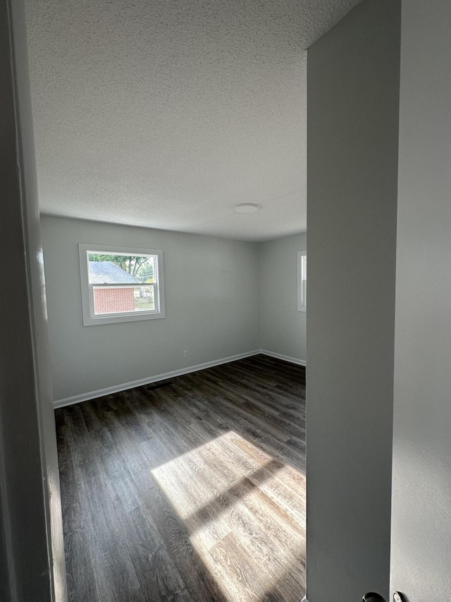 spare room featuring dark wood-style floors, a textured ceiling, and baseboards