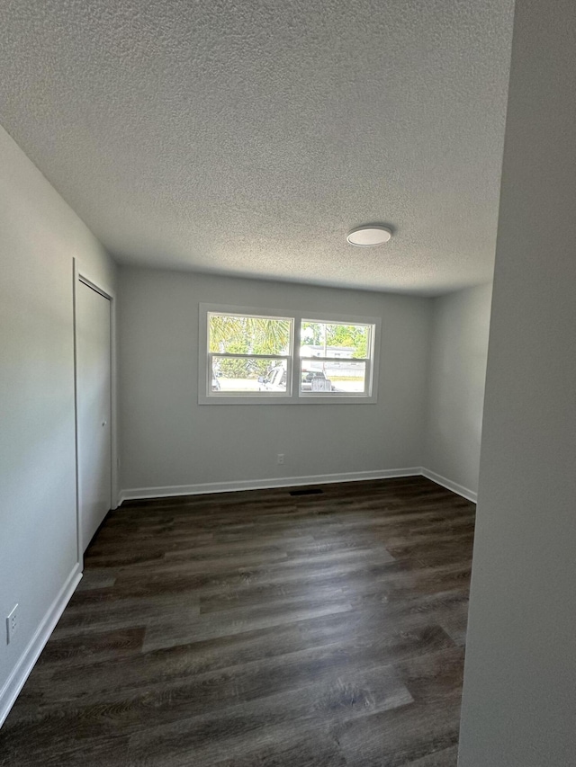 spare room with a textured ceiling, dark wood-style flooring, and baseboards