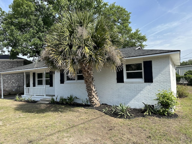 view of front of house with brick siding, a porch, a front yard, a carport, and a shingled roof