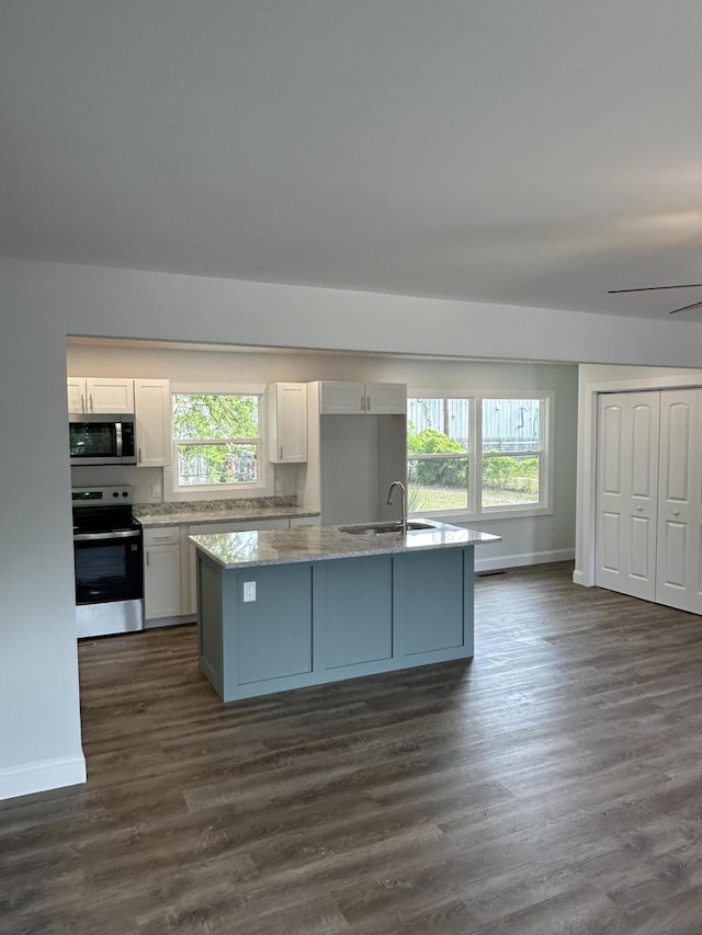 kitchen with stainless steel appliances, a sink, white cabinetry, a kitchen island with sink, and baseboards