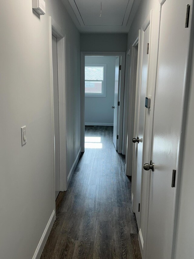 hallway featuring attic access, dark wood-style floors, and baseboards