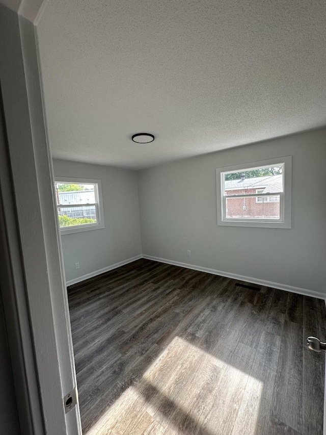 empty room featuring dark wood-type flooring, a textured ceiling, and baseboards