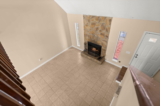 unfurnished living room featuring light tile patterned floors, a stone fireplace, baseboards, and lofted ceiling