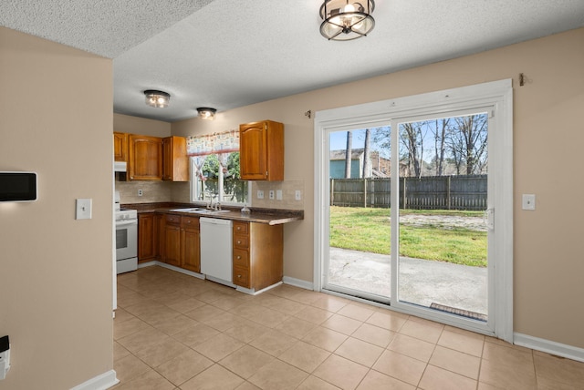 kitchen featuring white appliances, brown cabinetry, baseboards, a sink, and backsplash