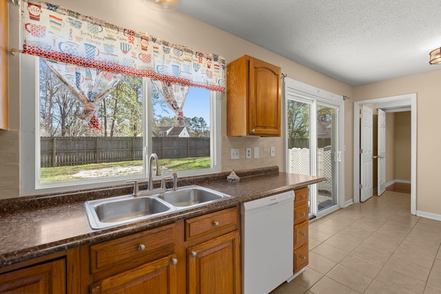 kitchen with dishwasher, dark countertops, brown cabinetry, and a sink