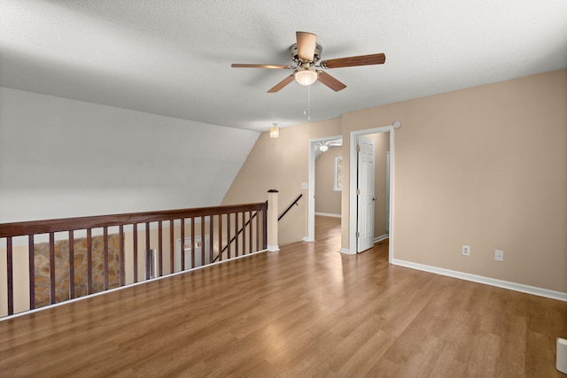 empty room featuring ceiling fan, a textured ceiling, baseboards, and wood finished floors