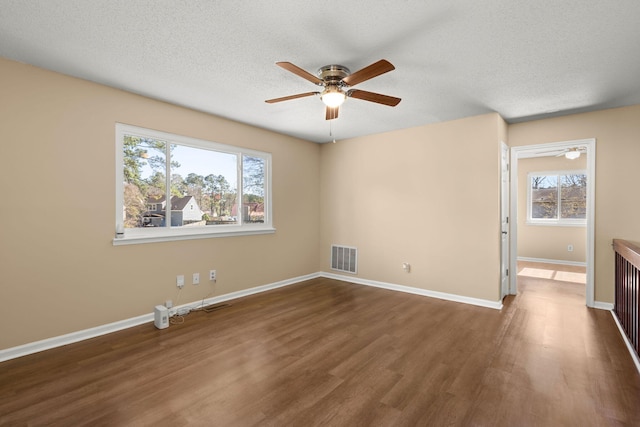 unfurnished room featuring a wealth of natural light, visible vents, baseboards, and dark wood-style flooring