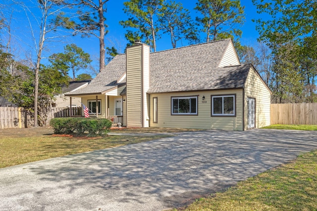 view of front of property with a front lawn, fence, covered porch, a shingled roof, and a chimney