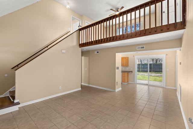 unfurnished living room featuring visible vents, a ceiling fan, a high ceiling, light tile patterned floors, and stairs