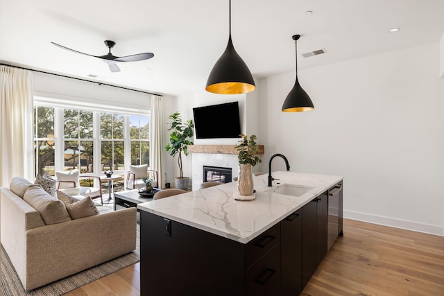living area featuring a high end fireplace, light wood-type flooring, a ceiling fan, visible vents, and baseboards