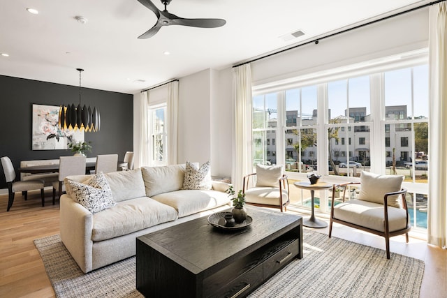 living area featuring visible vents, light wood-type flooring, recessed lighting, and ceiling fan with notable chandelier