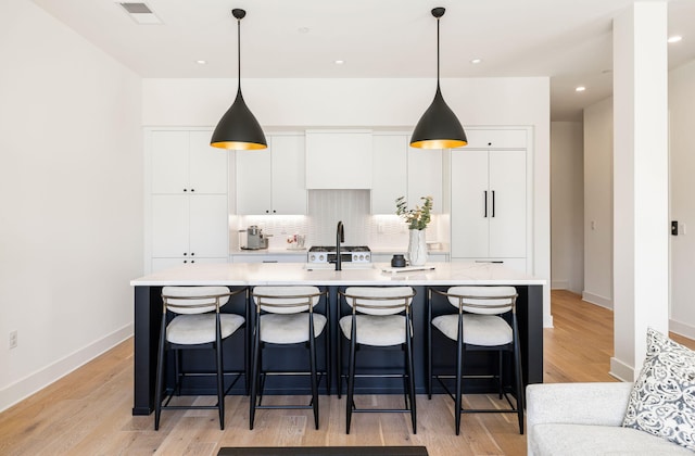 kitchen featuring an island with sink, white cabinetry, visible vents, light countertops, and decorative backsplash