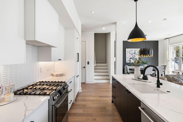kitchen with white cabinets, a sink, stainless steel appliances, backsplash, and light wood-style flooring