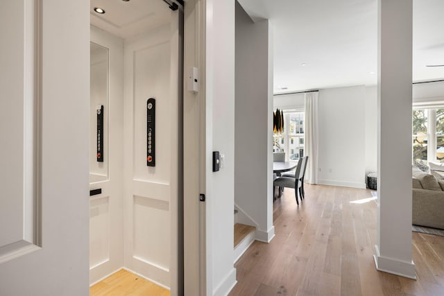 hallway featuring light wood-type flooring, baseboards, and elevator