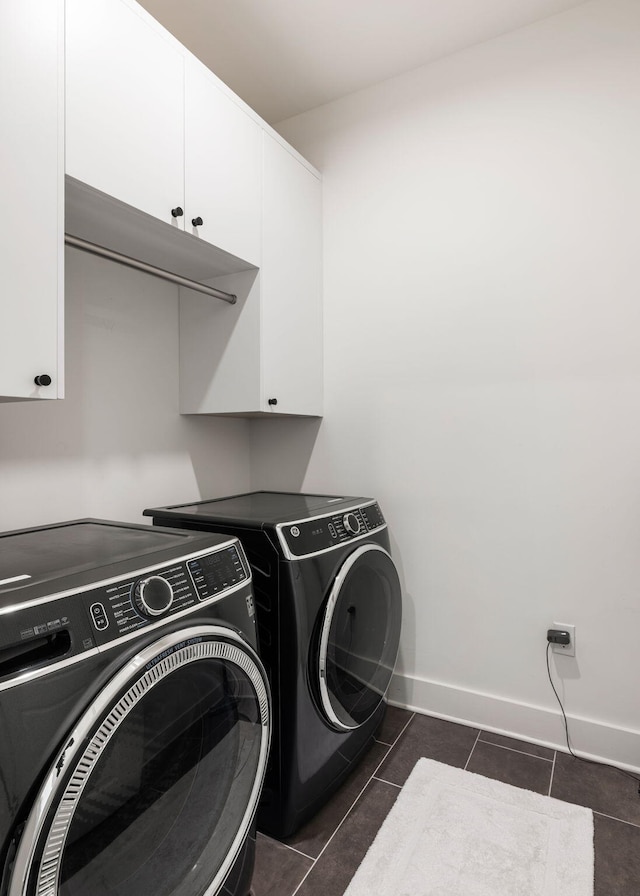 laundry room featuring cabinet space, dark tile patterned flooring, washing machine and clothes dryer, and baseboards